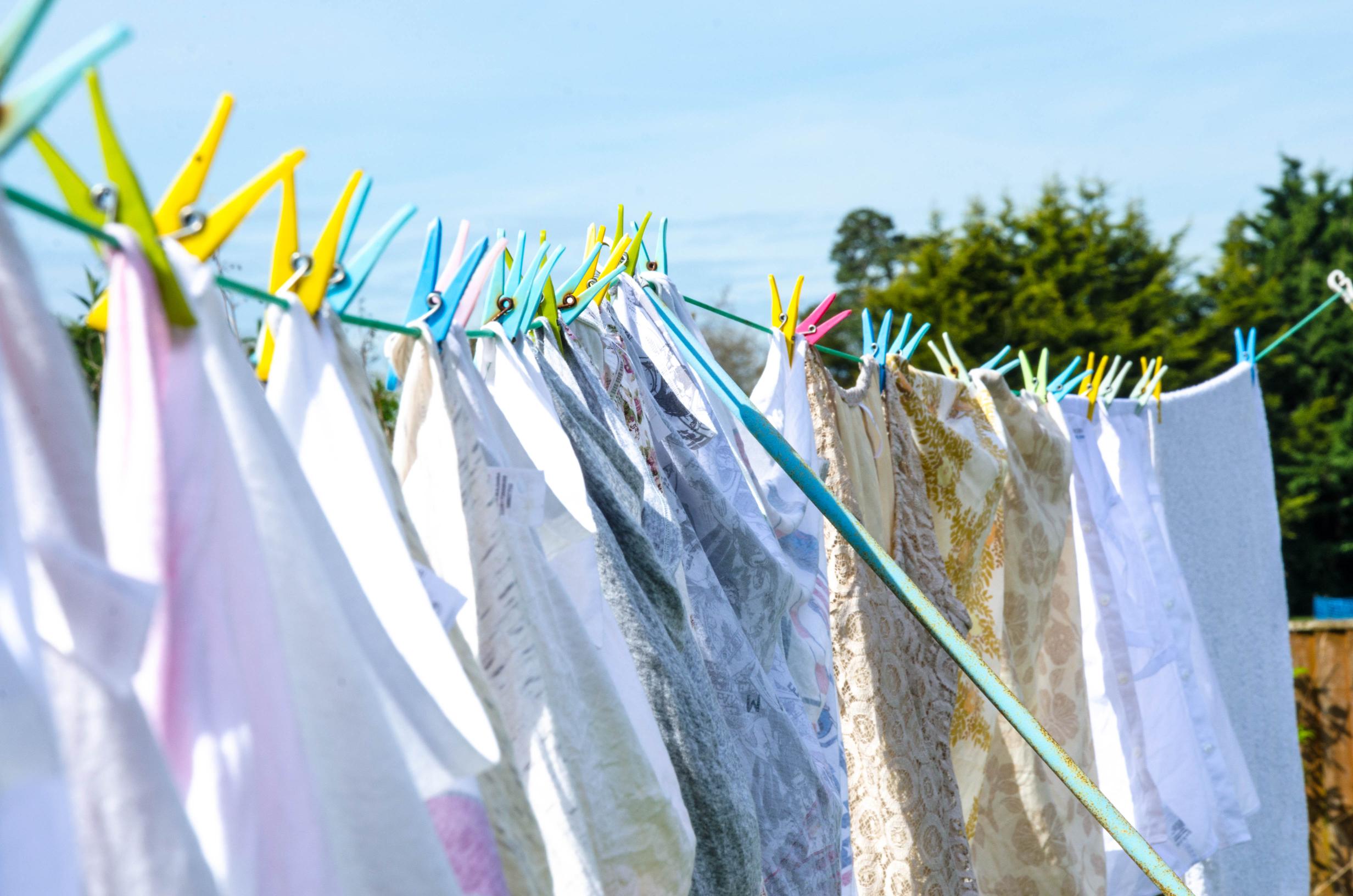 Linge suspendu à une corde à linge avec des pinces colorées, séchant à l'air libre sous un ciel ensoleillé.