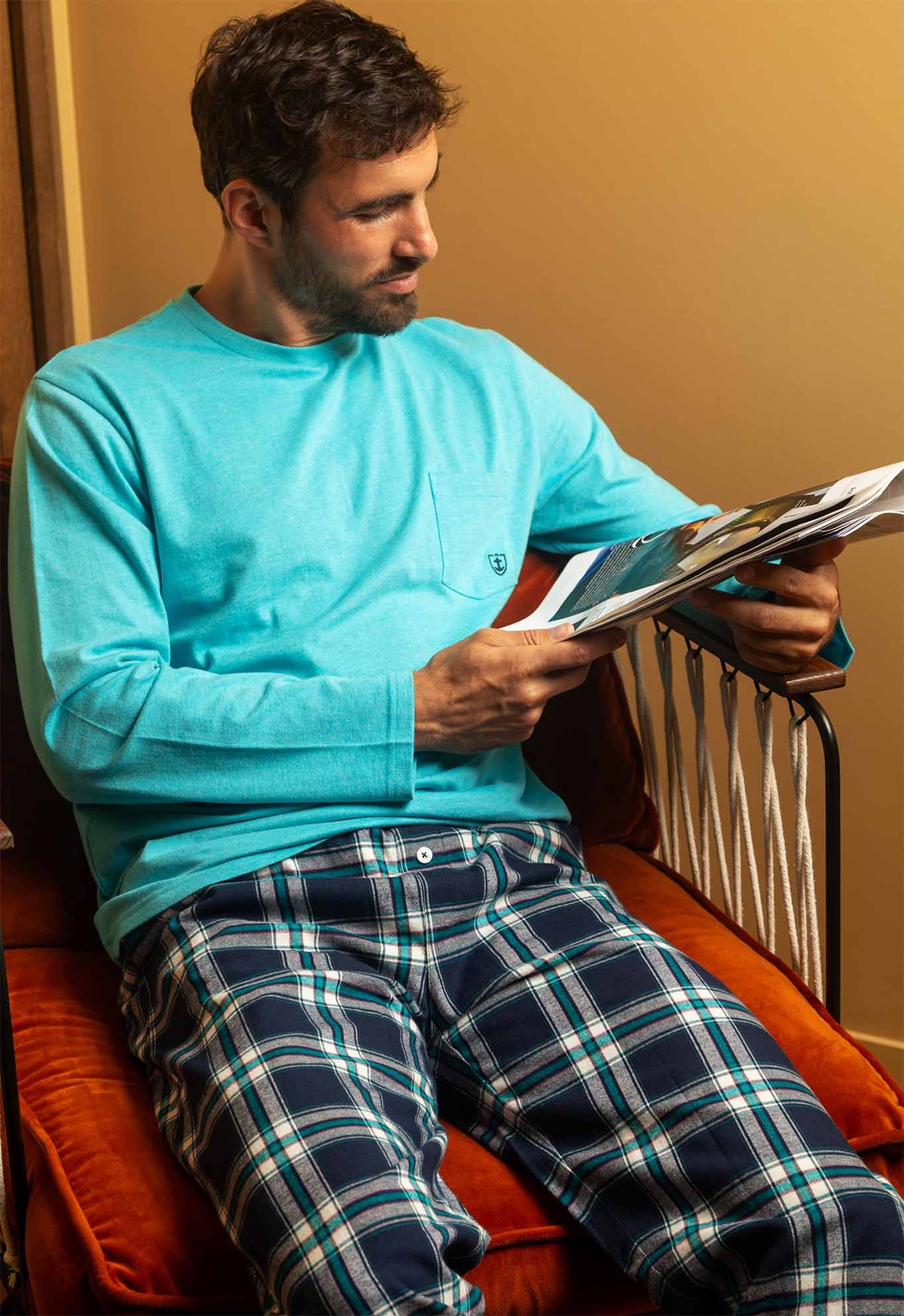 Homme en pyjama à carreaux bi-matière, haut en jersey bleu pétrole et pantalon écossais, lisant dans un fauteuil