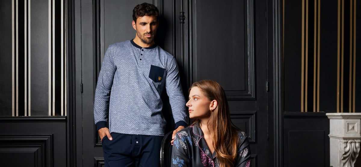L'homme porte un pyjama bleu avec un haut à col rond et poche contrastée, tandis que la femme est assise,